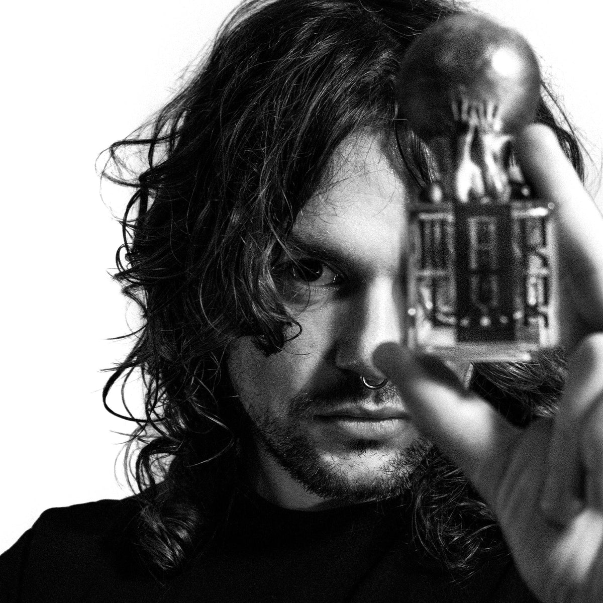 Man with long hair holding artistic perfume bottle in black and white portrait